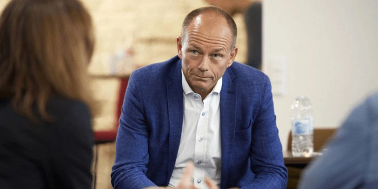 En mand i skjorte og en blå blazerjakke sidder overfor en kvinde